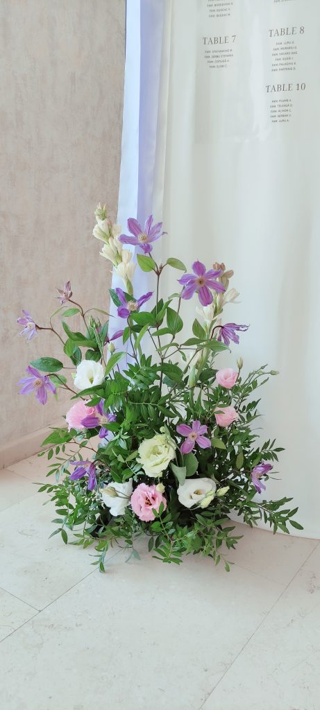 Aranjament floral cu clematis lila, trandafiri și verdeață la baza panoului, nuntă Iași